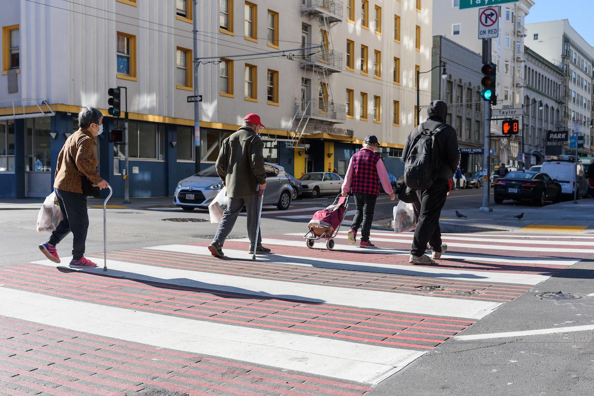 A group of people cross the street on a red and white striped crosswalk.
