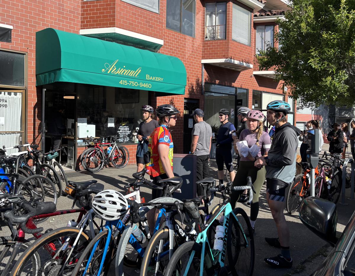 People with bicycles in front of a building near a tree.