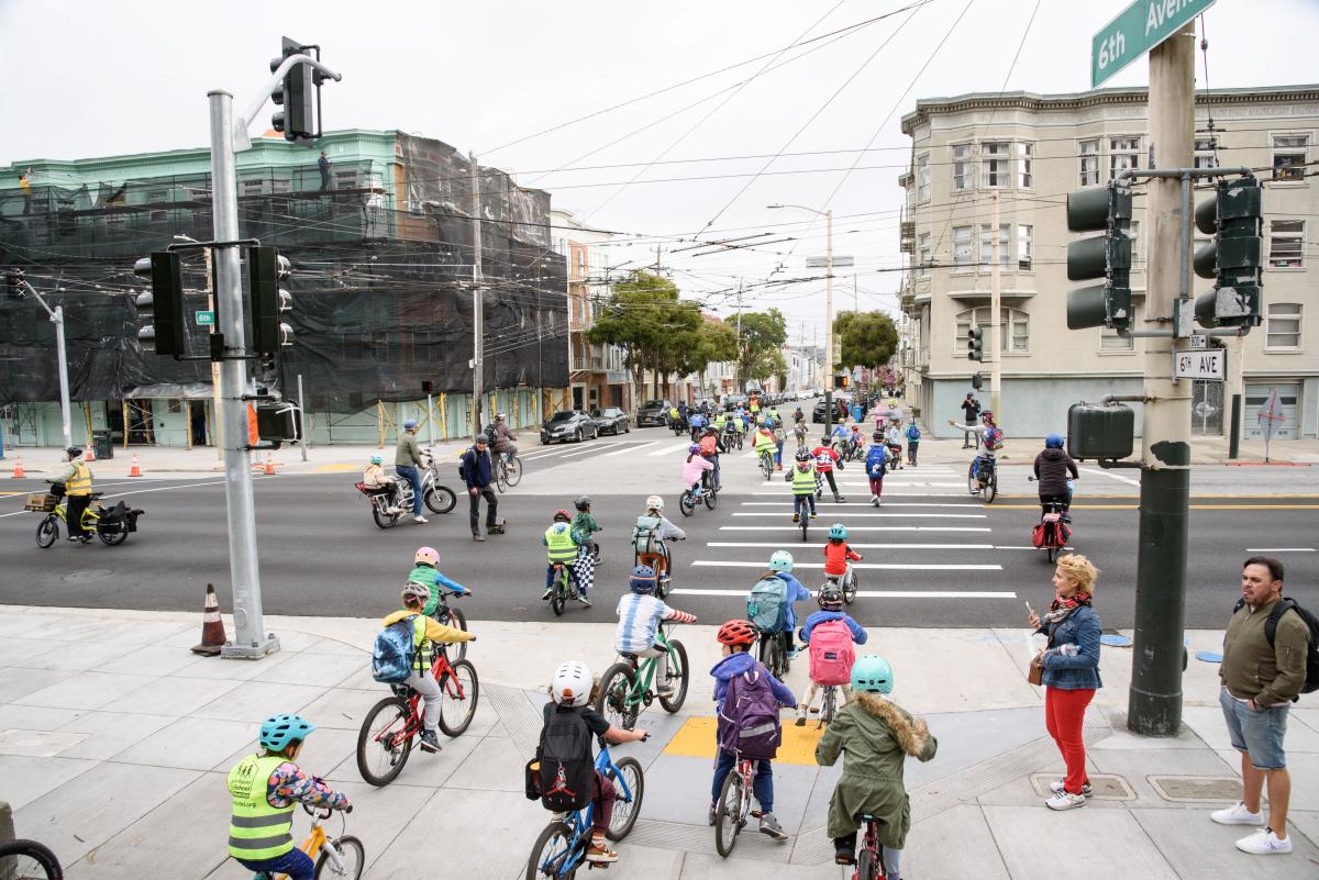 Children on bikes on the sidewalk and in the crosswalk.