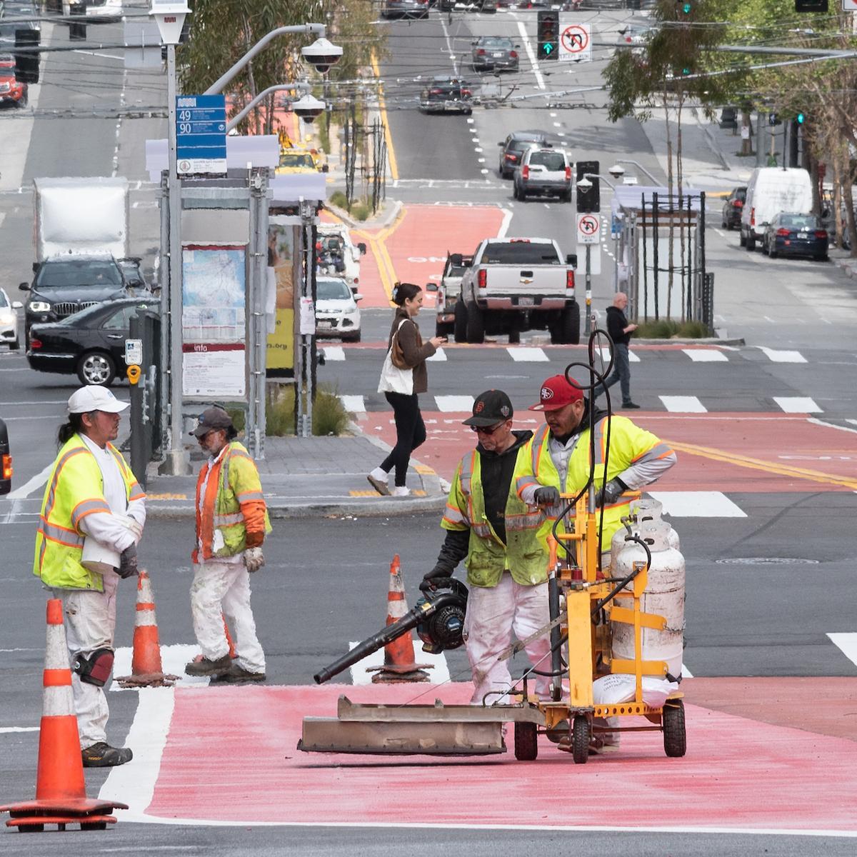 SFMTA crews in yellow safety vests work on a dedicated transit lane on Van Ness Avenue.