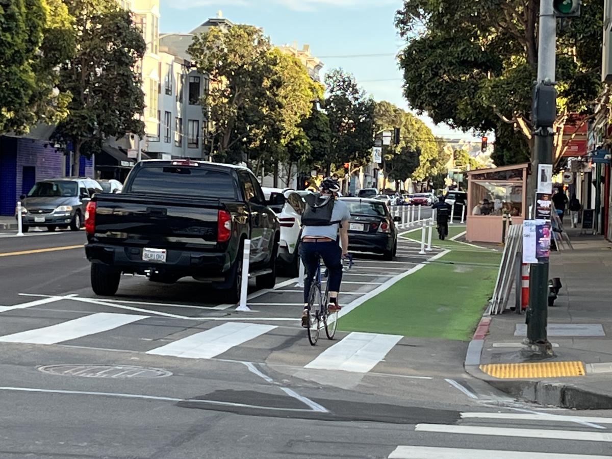 Person bikes toward a green side-running protected bikeway on Valencia Street.