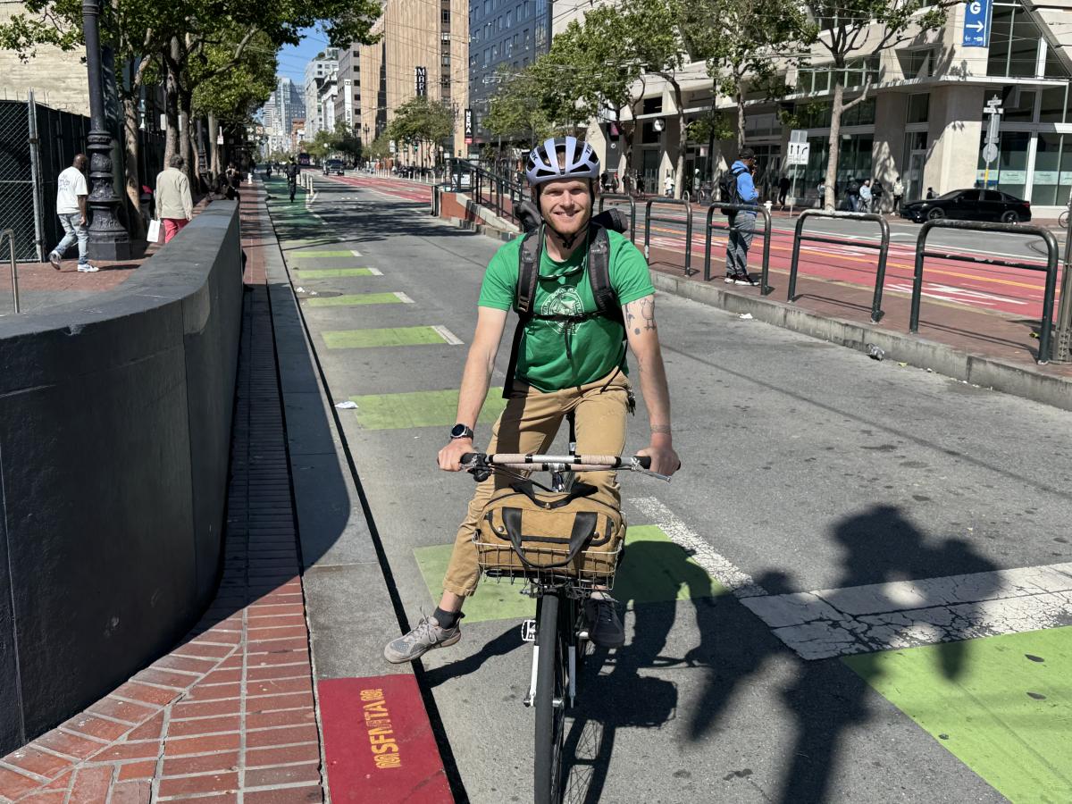 Person stops at a curb on Market Street from the protected bikeway and smiles for a photo. 