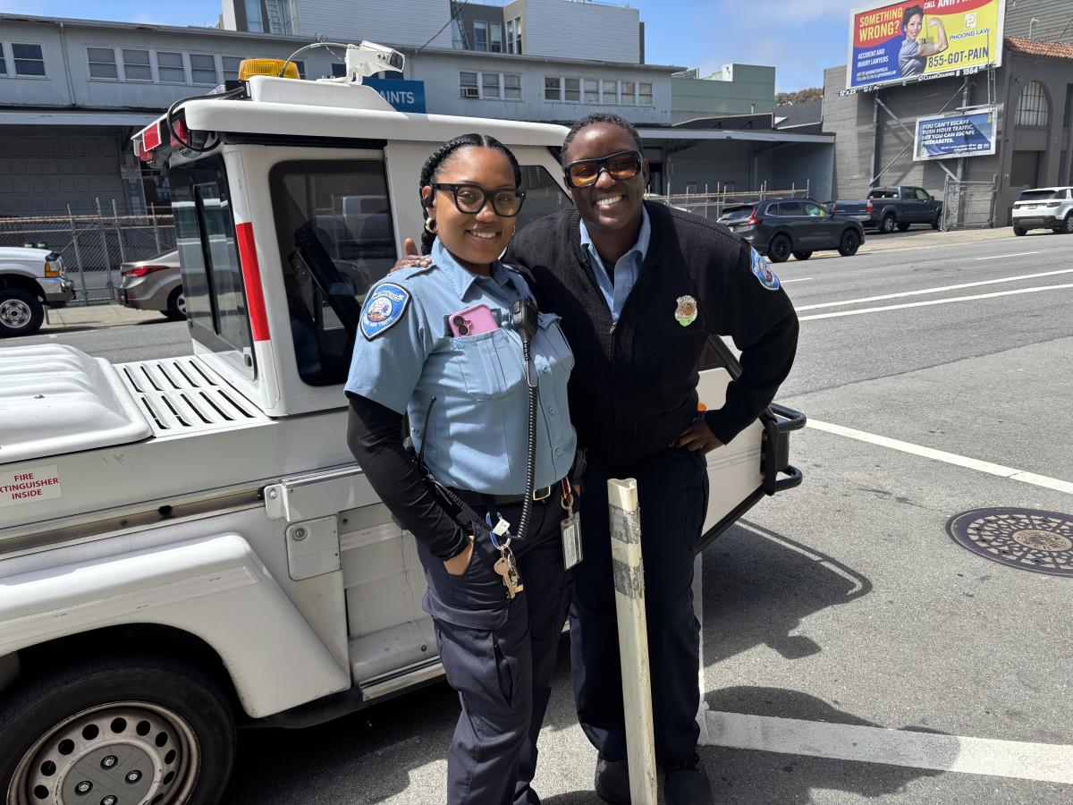 Two people standing in front of a vehicle on the street.