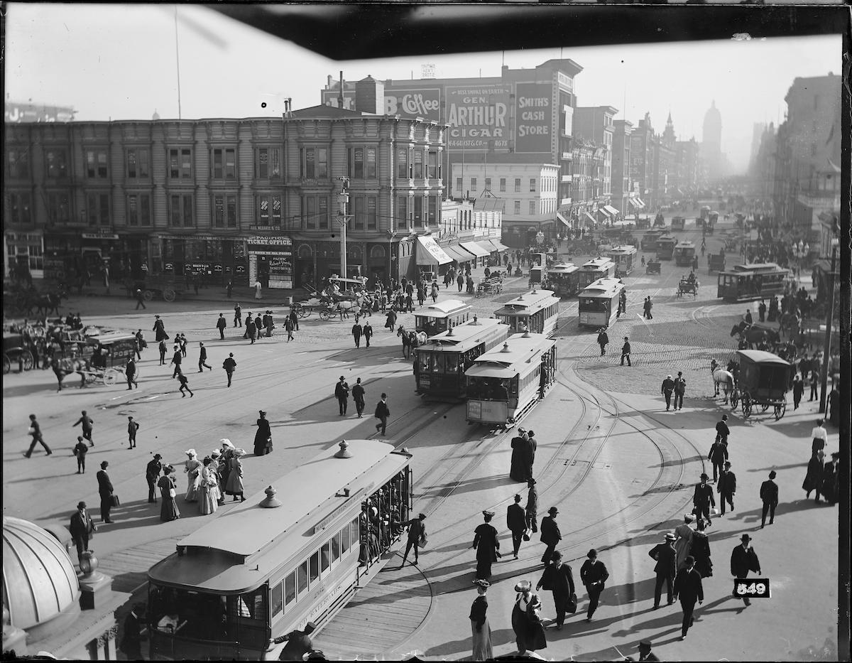 Black and white photo from 1905 showing cable cars and dozens of people walking in downtown San Francisco near the Ferry Building.