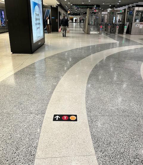 Image of Powell Station's floor with a small sign that has an arrow, a T Third logo and an image of a basketball.