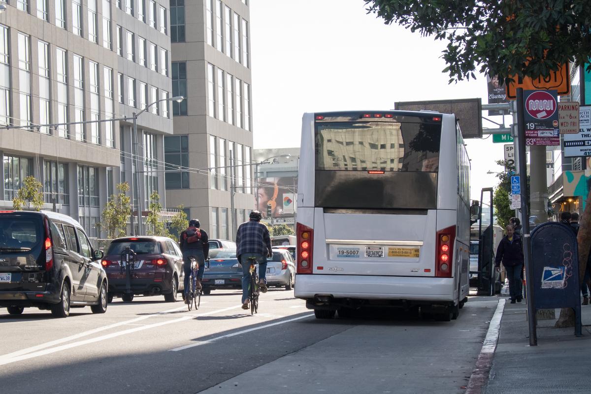 Two people bike past a commuter shuttle on a city street.