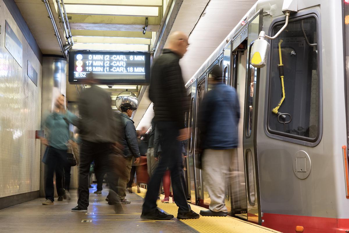 People board and exit on a Muni Metro train at a station platform.