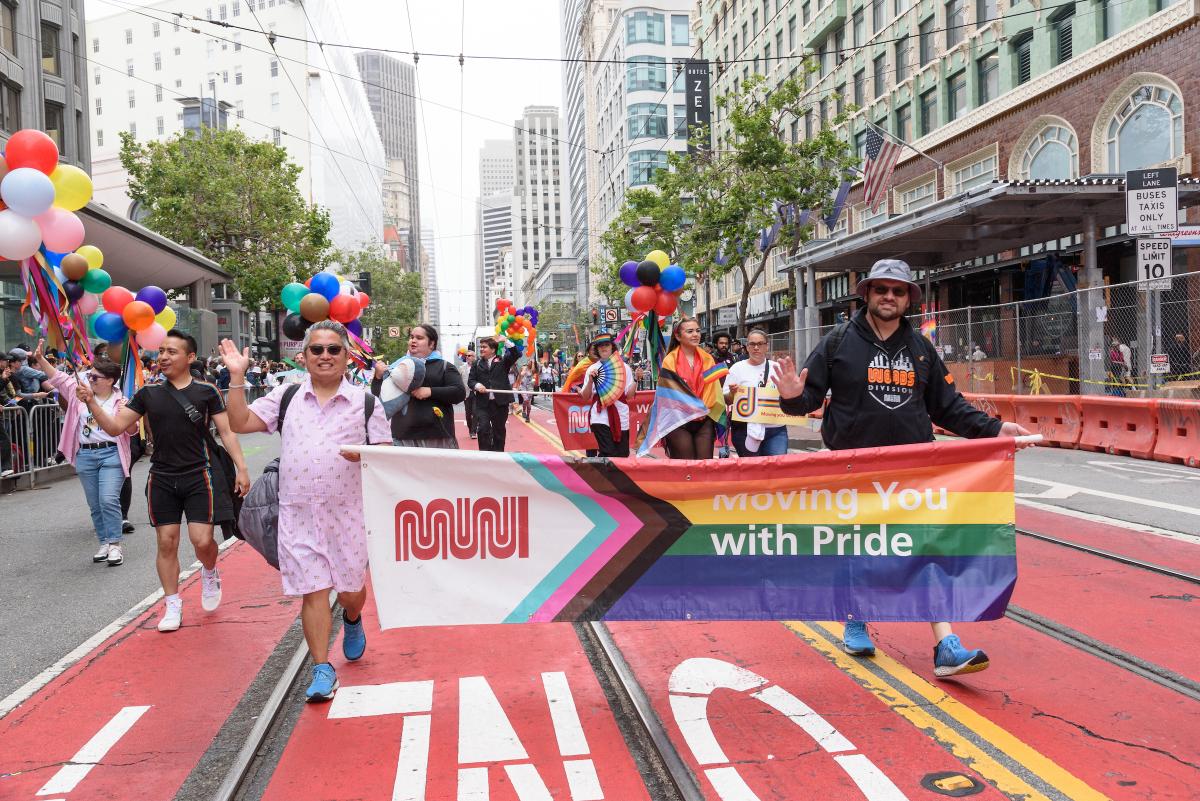 SFMTA contingent at last year's Pride Parade. People hold a banner that has the Muni logo and part of the rainbow flag.