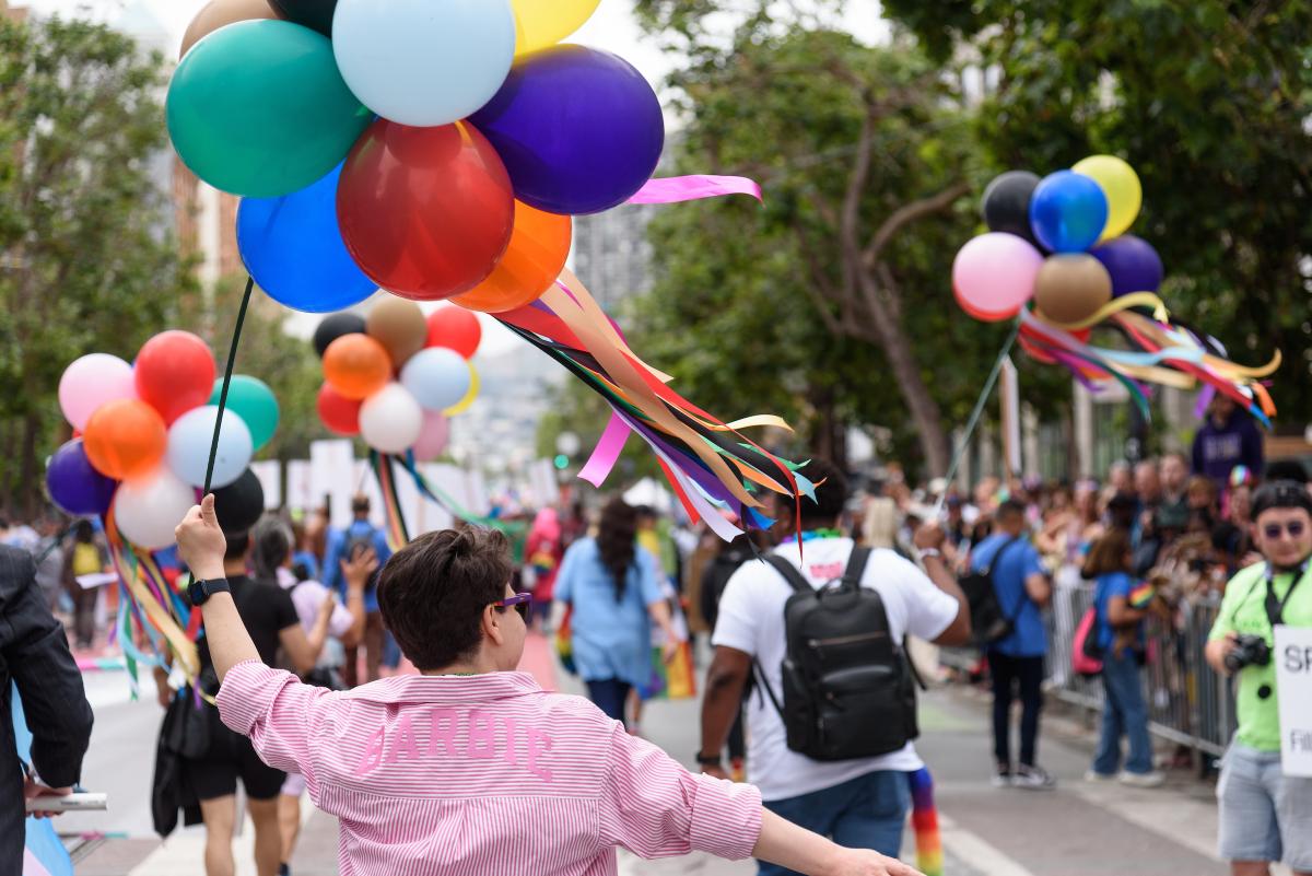 Person holds colorful balloons while walking in the 2024 Pride Parade near other attendees.