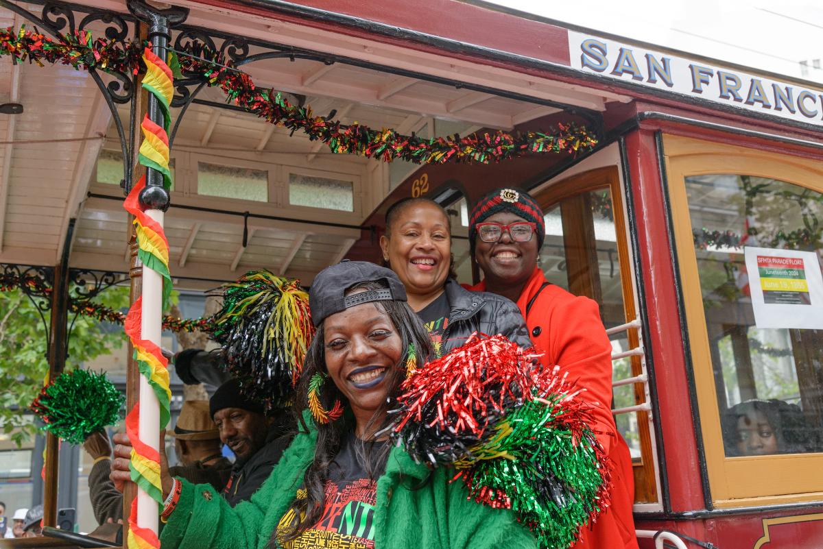 Three people smile from a motorized cable car that's decorated with Juneteenth colors during last year's parade.