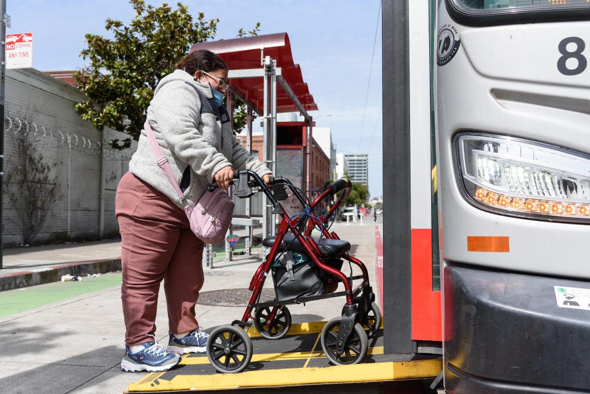 Person using a mobility device steps on a Muni ramp to enter a bus. 