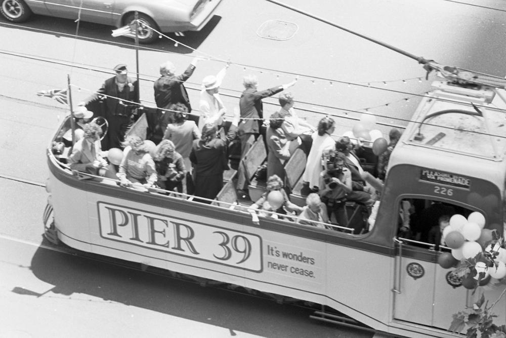 Black and white photo of a Boat Tram historic streetcar with people waving.