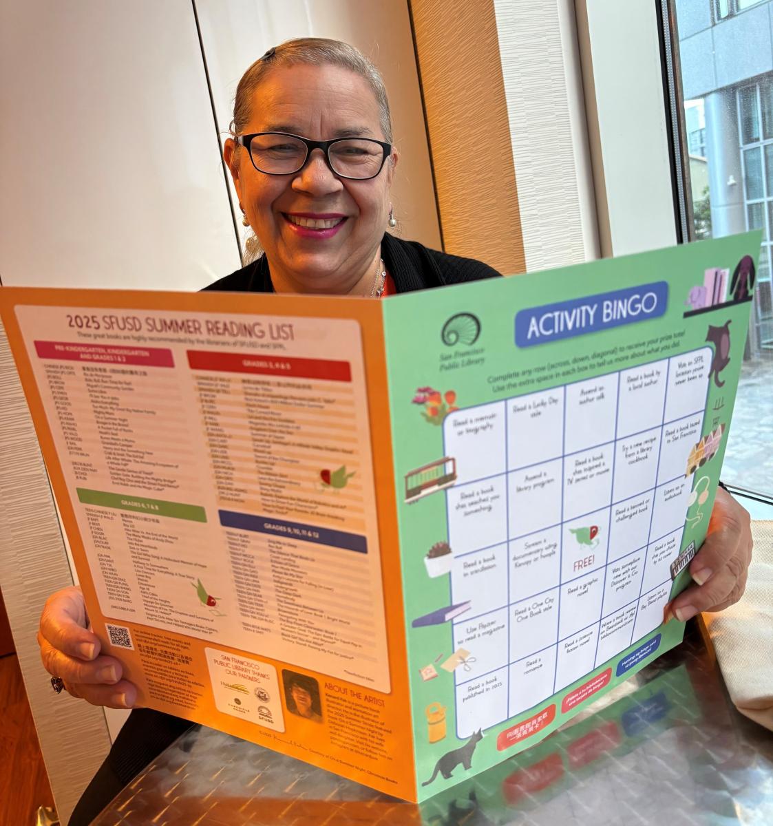 Person smiles while holding a large, multi-colored activity bingo card.