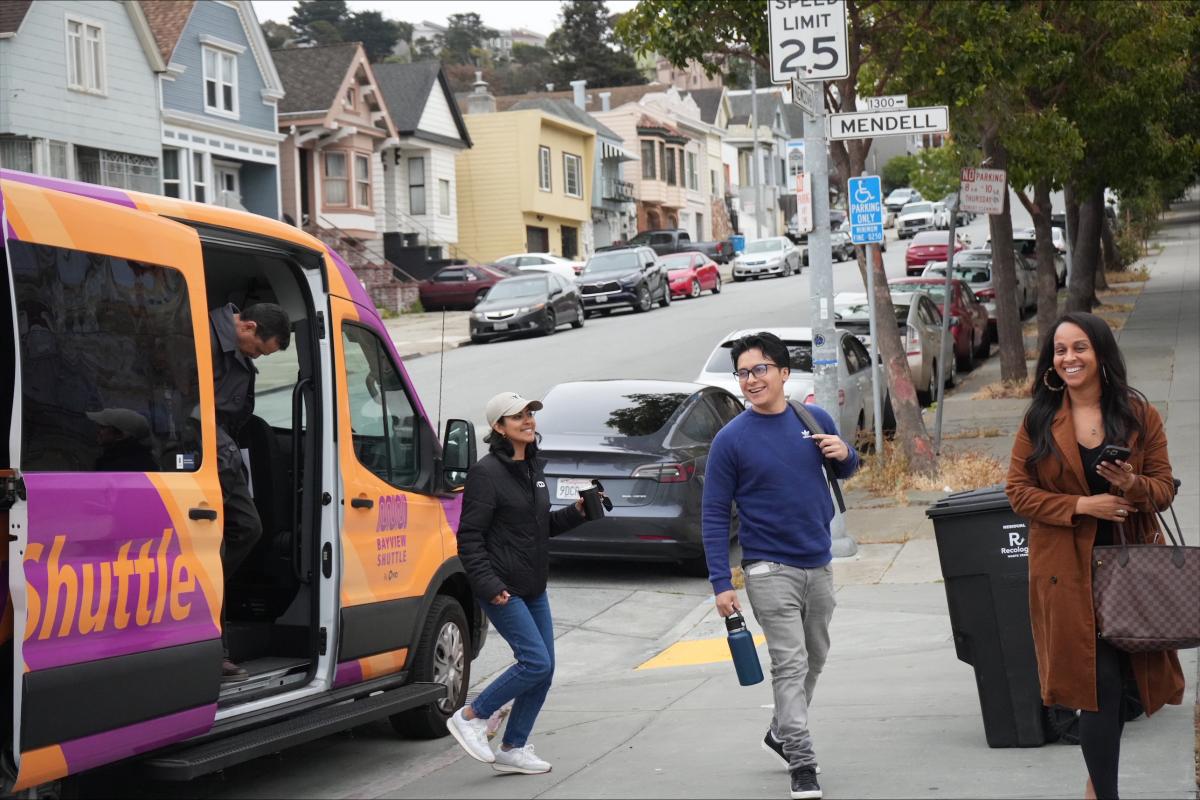 Three people exit an orange and purple Bayview Shuttle. 