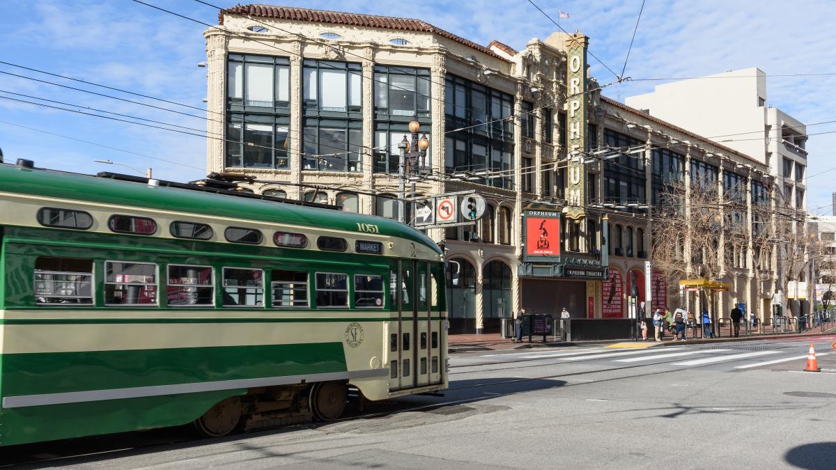 F Market streetcar that's green and cream heads downtown approaching the Orpheum Theatre.