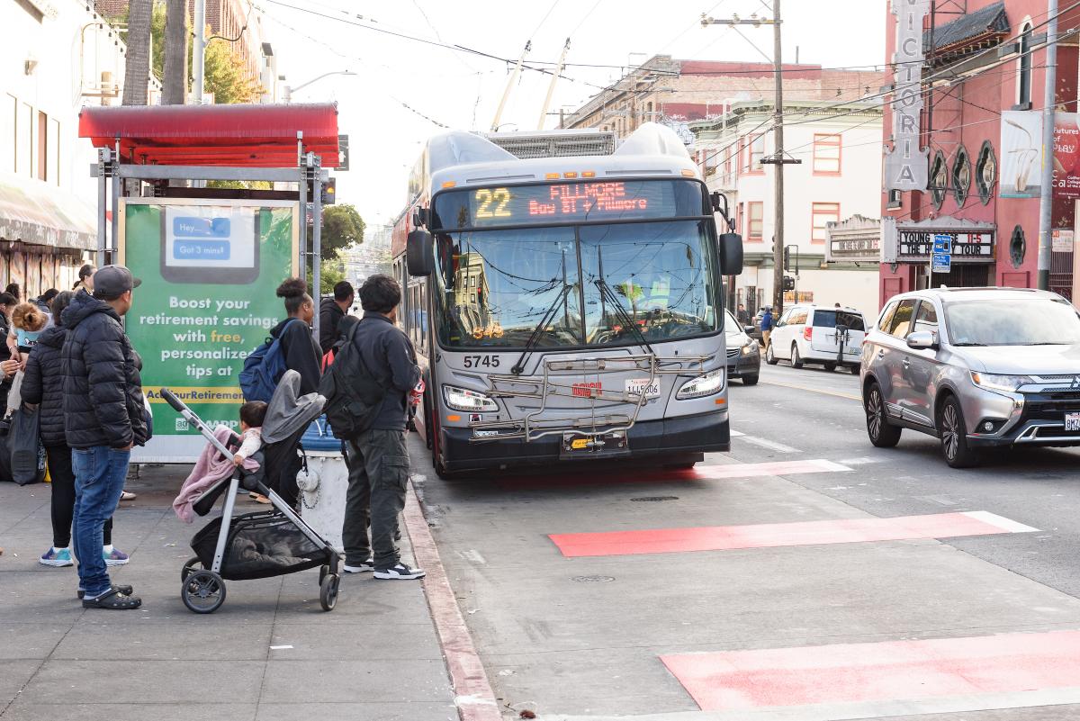 Several people wait to board a 22 Fillmore near a dedicated transit lane.