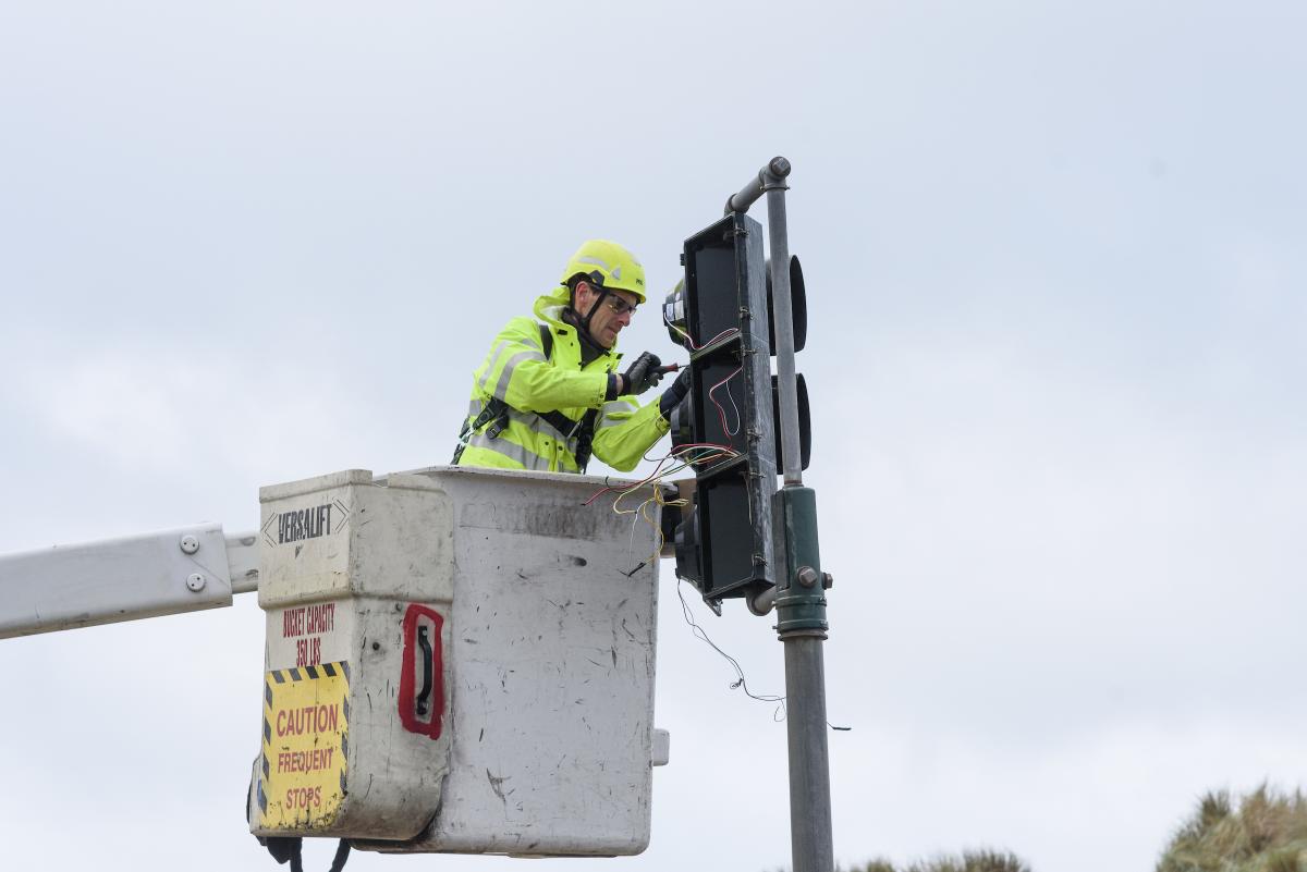 Person in a yellow vest and helmet installs a new traffic light in the Outer Sunset for the Great Highway road closure.