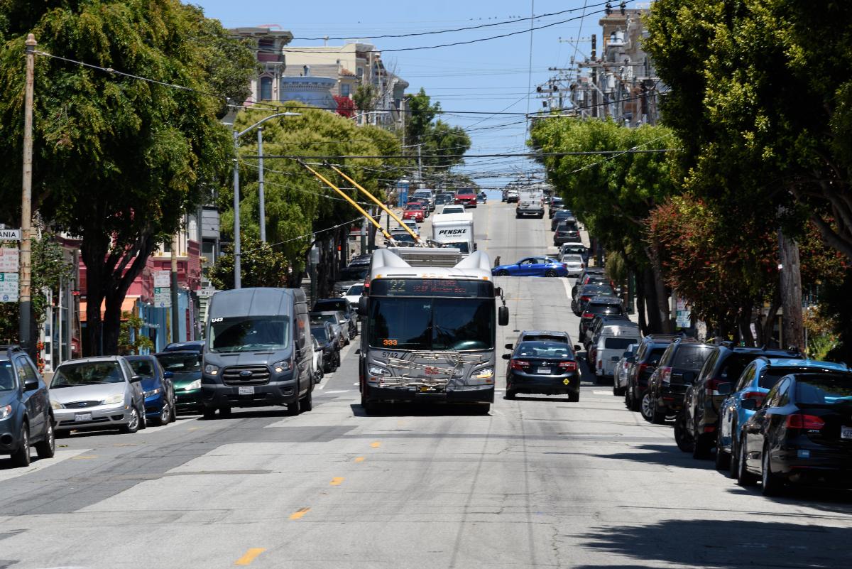 22 Fillmore bus drives around a double parked car on a city street.