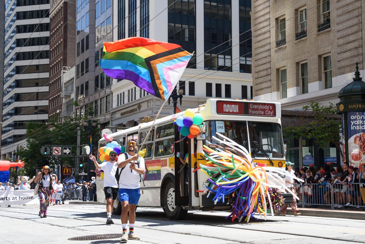 People wave a rainbow flag near a Muni bus decorated for the San Francisco Pride Parade.