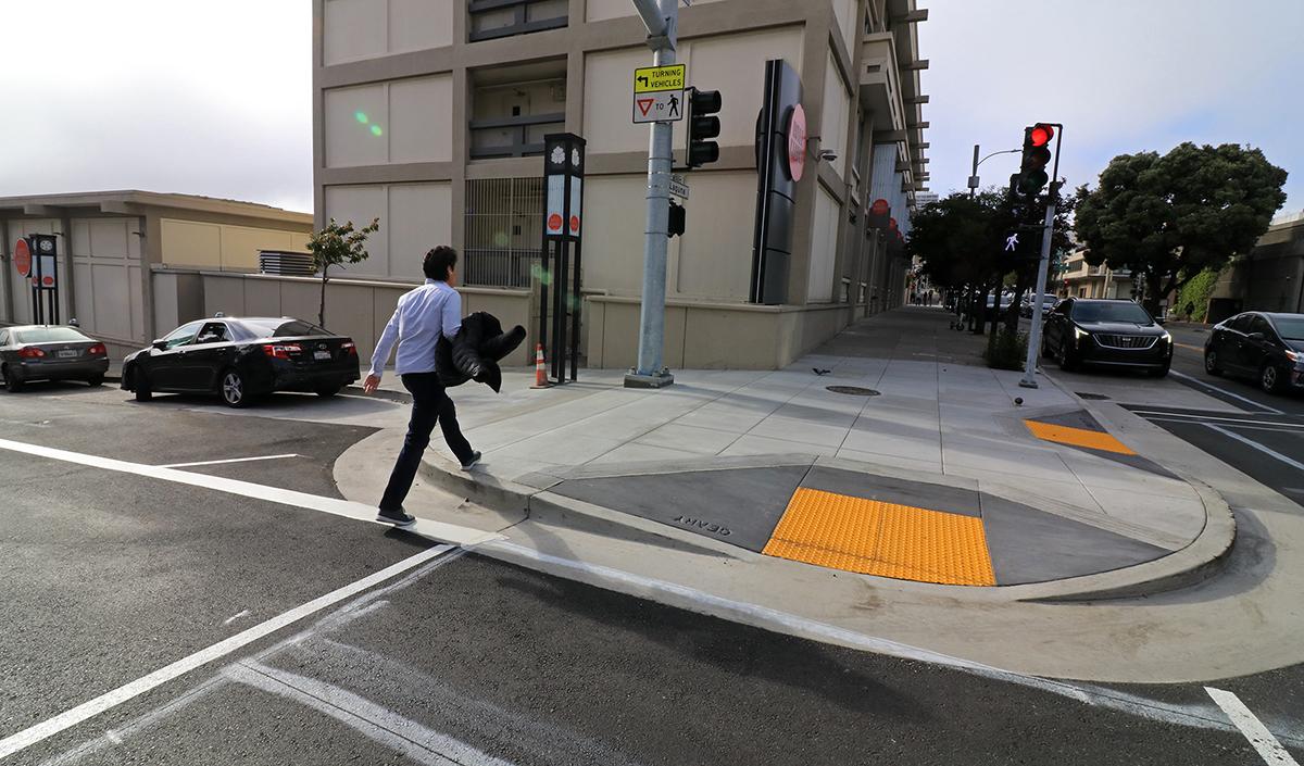Person walks onto a pedestrian bulb-out on Geary. This infrastructure extends the sidewalk into the crosswalk.