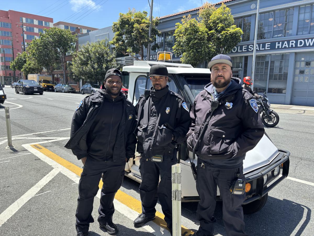 Three men standing in front of a small white vehicle.
