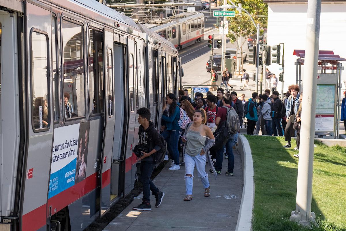 Teenagers getting on a train at a transit stop.