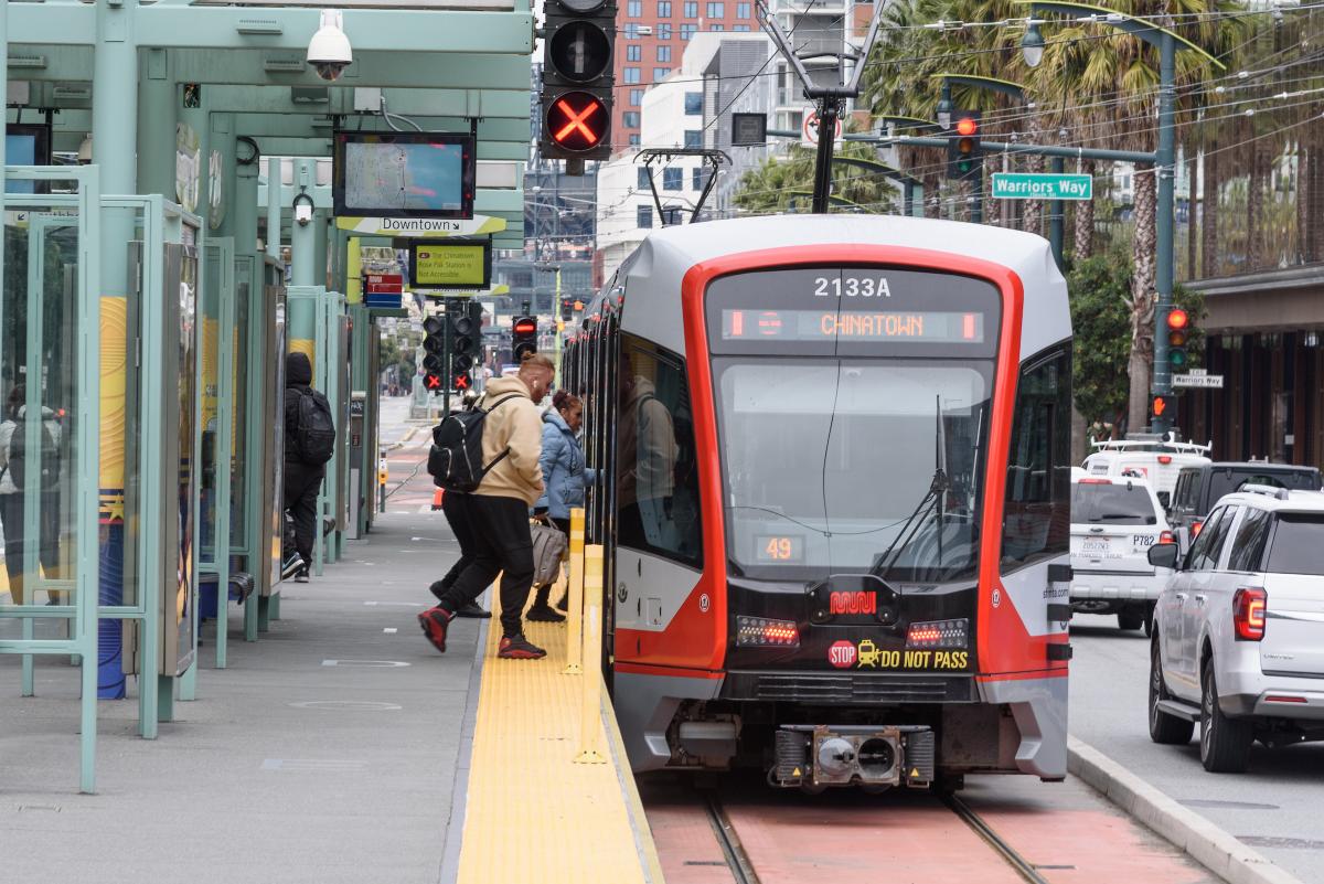 People board a T Third Train on an outdoor platform. 