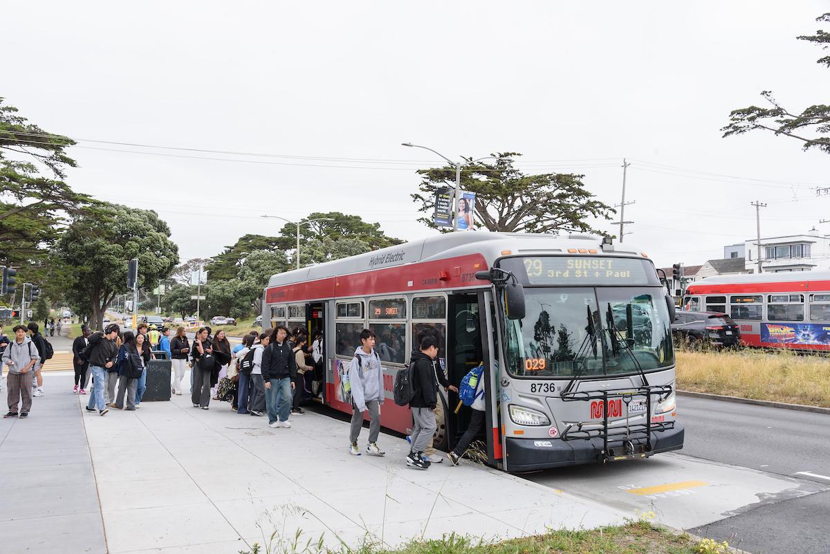 Kids and young teenagers getting onto a bus at the sidewalk.