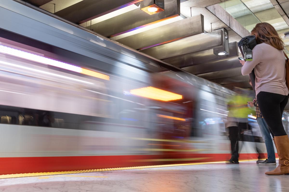 Train passes by in a blur as a person waits on a Muni Metro platform.