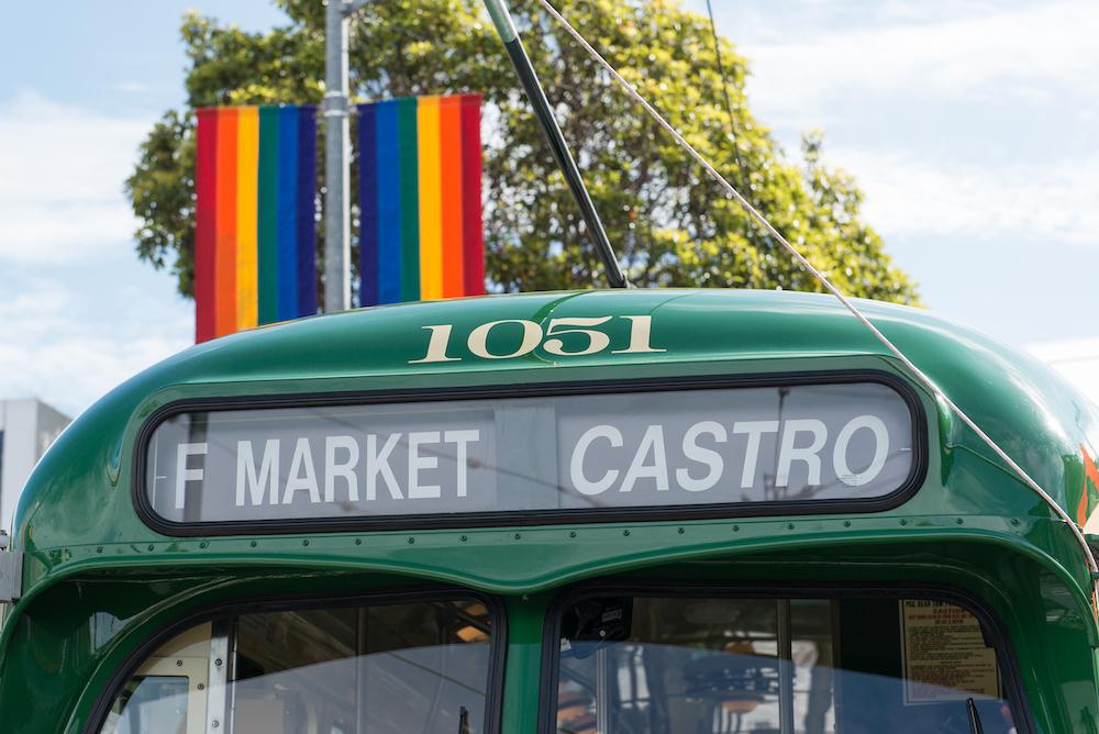 Closeup of an F Market streetcar showing the vehicle name and destination with a rainbow flag in the background.