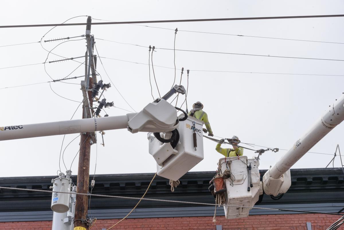 Crews use machinery to work high up near utility poles and overhead lines.