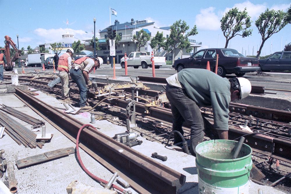 Construction worker reaches down to set rails for the F on a curved part of the route.