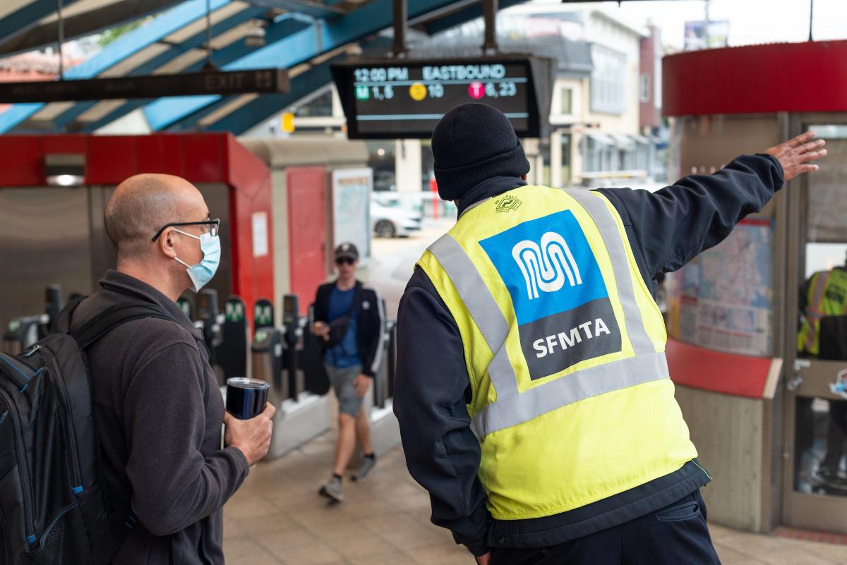 A station agent wearing a yellow vest helps a rider with directions.