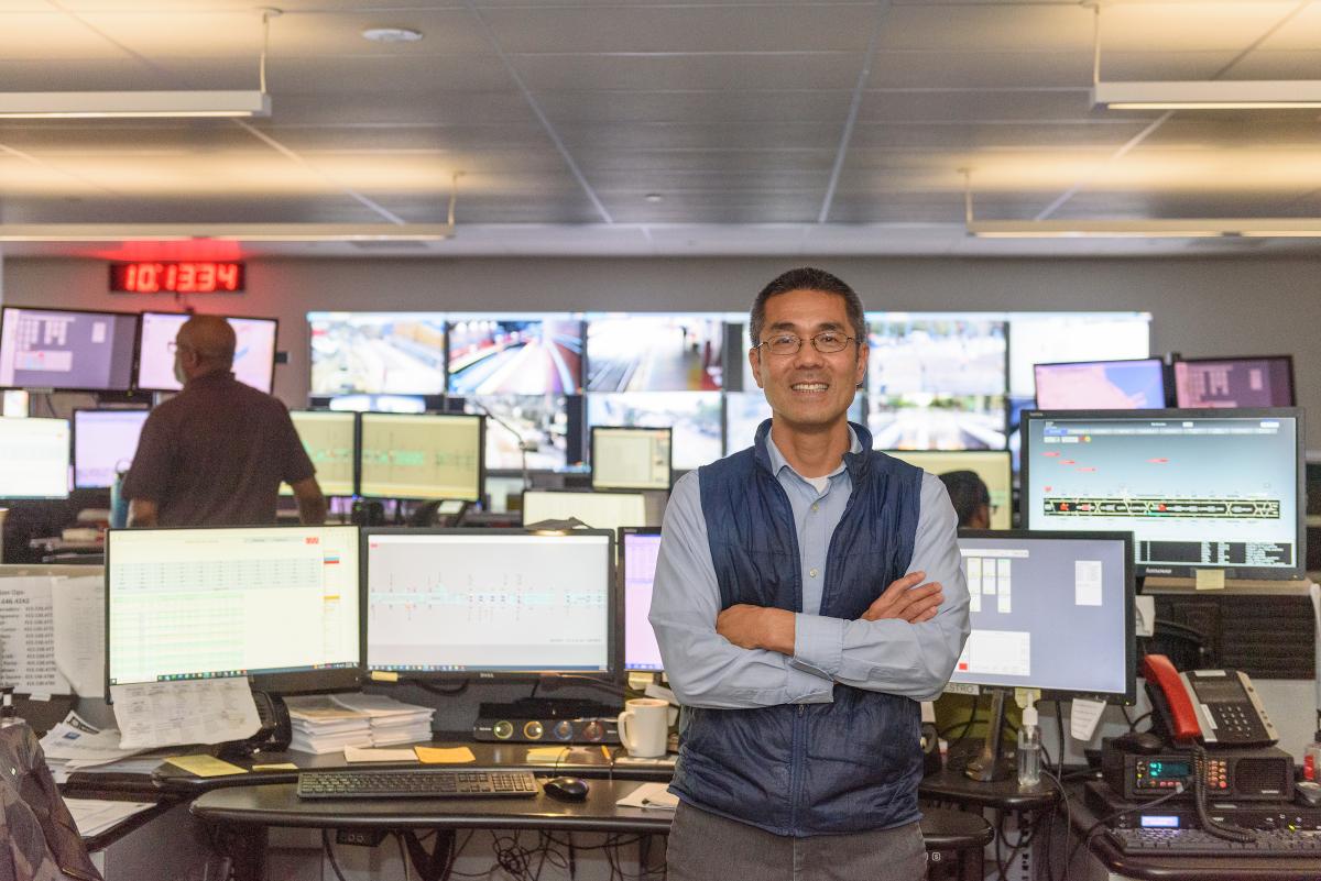Transportation Management Center staff member poses for a photo near several computer and TV screens.