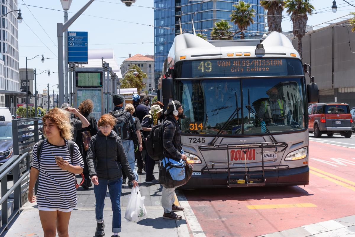 People boarding and exiting a 49 Van Ness bus parked in a dedicated transit lane.