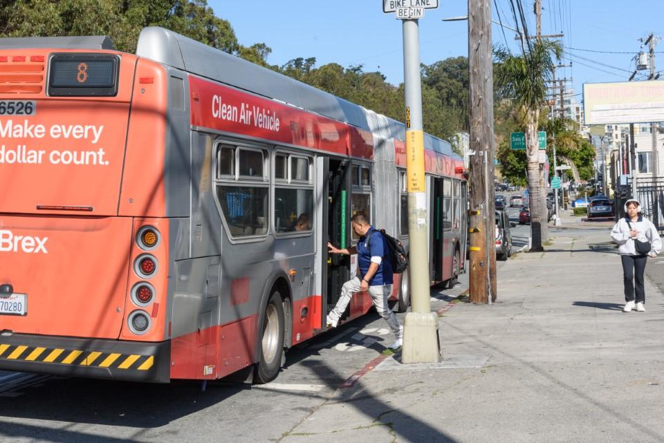 Person boards an 8 Bayshore bus while someone walks nearby on a sidewalk.