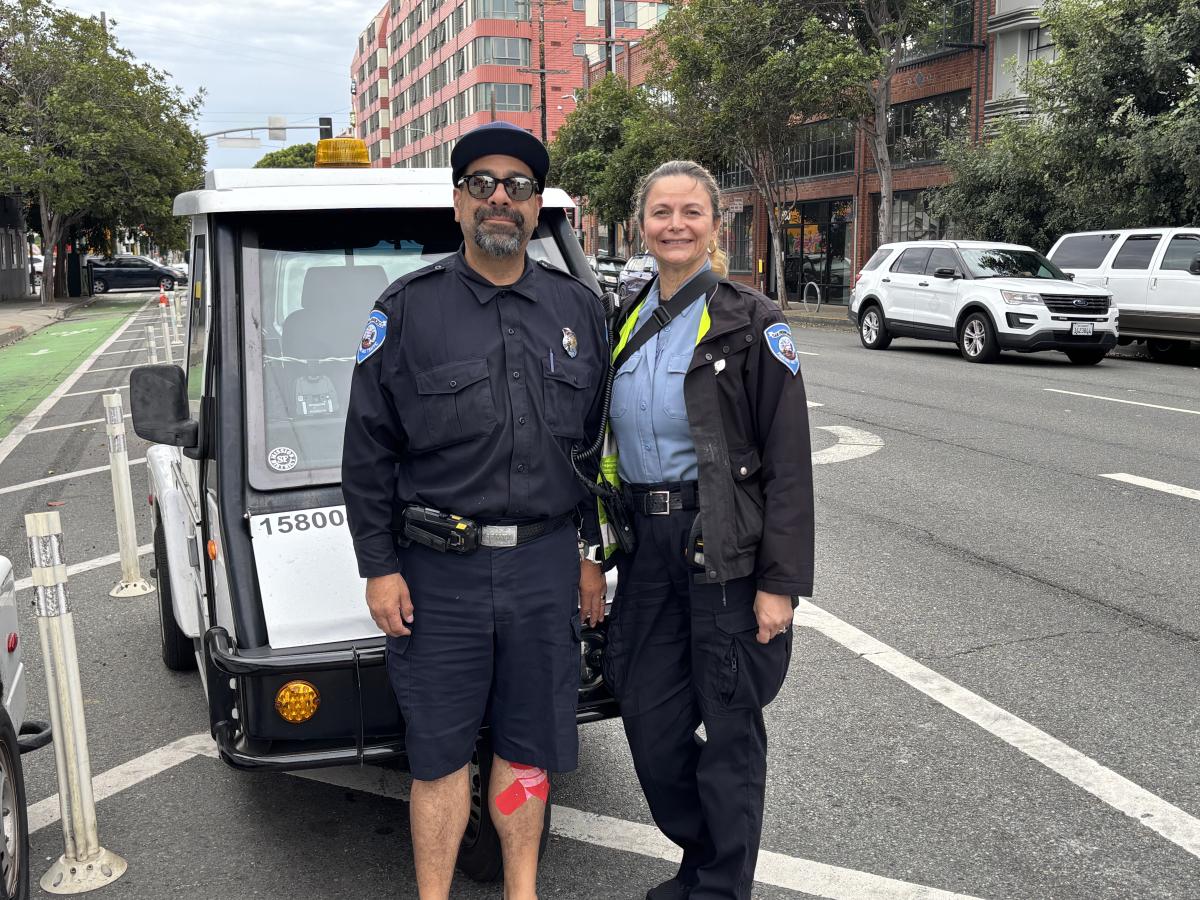 Two people standing in the street in front of a small vehicle.