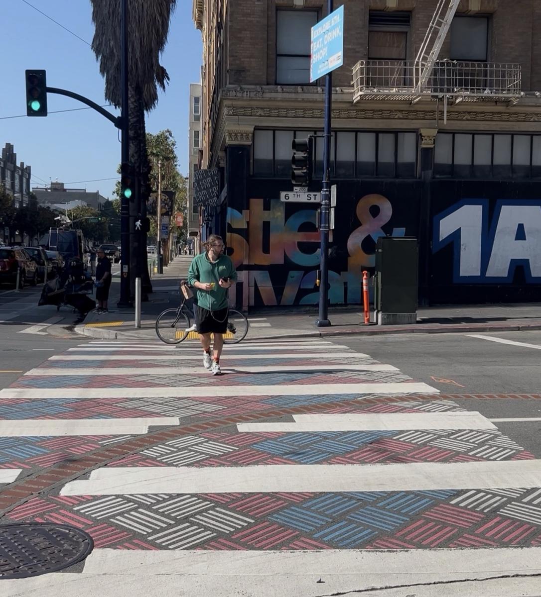 Person walking on a new decorative sidewalk on 6th Street. Crosswalk features a red, white and blue design.