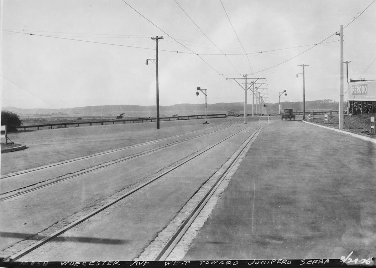 Black and white photo from 1936 showing an empty field served by the M line. A car drives in the distance.