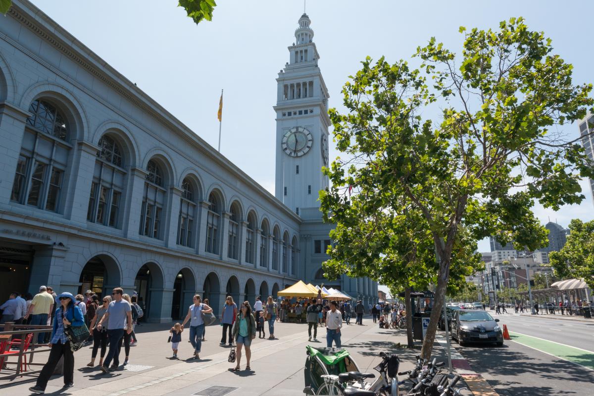 A photo of people walking in front of The Ferry Building along the Embarcadero in San Francisco, with The Ferry Building clock tower visible in the background.