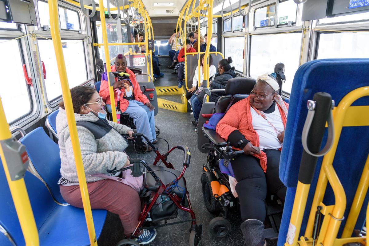 Two riders using mobility devices interact on a Muni bus. 