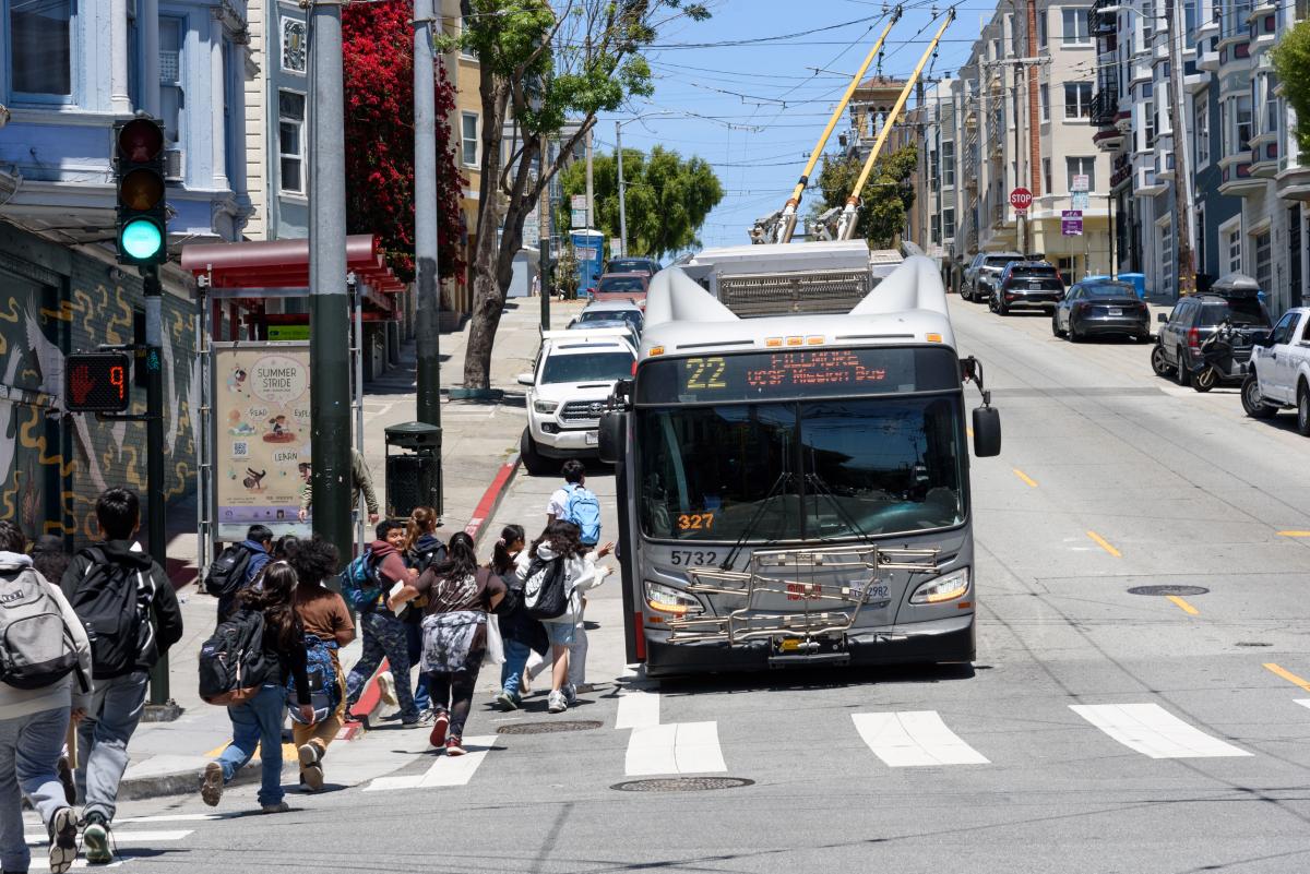 Several people walk to a 22 Fillmore stop to board a bus.