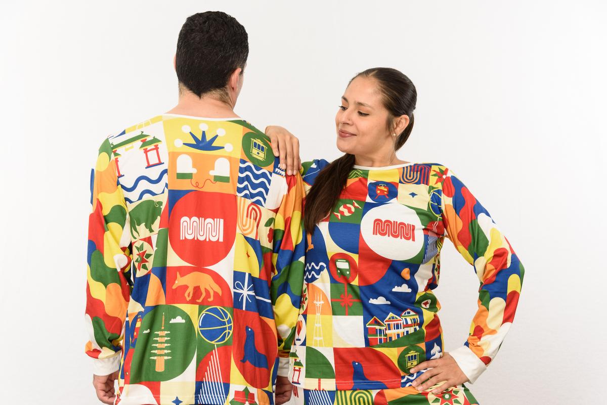 Two people pose in Patchwork of the City Holiday Pajama Sets. One person's back faces the camera.