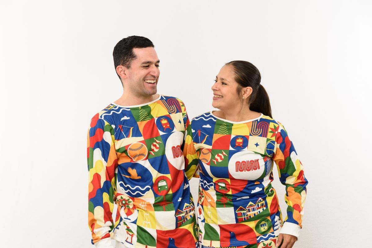 Two people laugh and smile as they pose in Merry Days of Muni Holiday Pajama Sets.