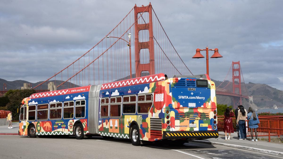 Bus wrapped with Merry Days of Muni stops in front of the Golden Gate Bridge.