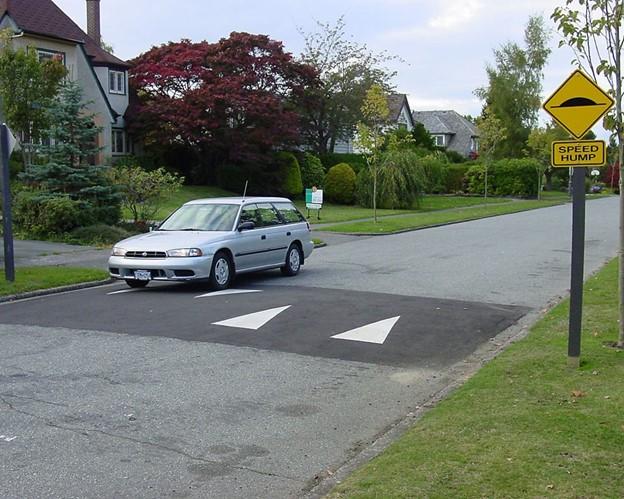 A car drives toward a traffic calming device -- a raised, marked area of the street. 
