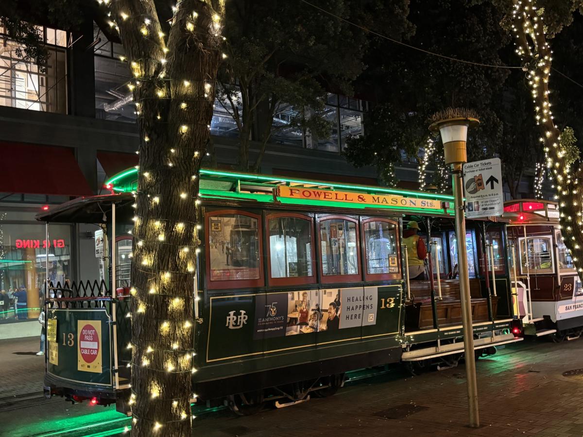 A cable car parked behind trees decorated with lights.