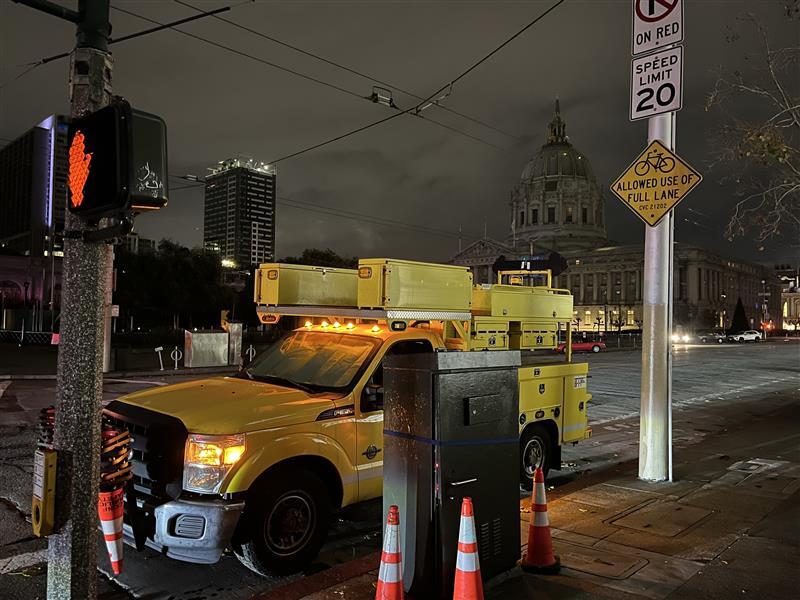 Yellow truck near electrical boxes on a downtown street.