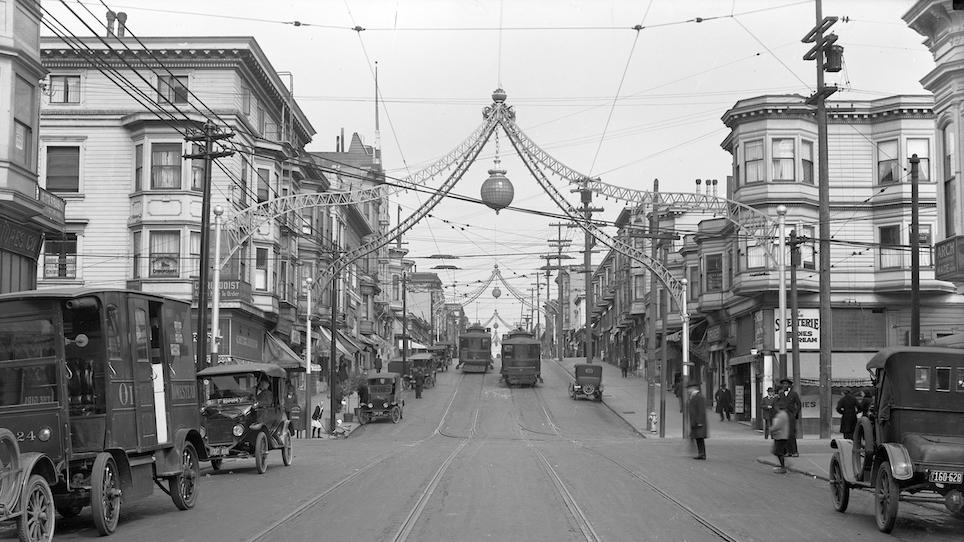Black and white photo from 1920 showing Fillmore Street with various vehicles in the road and people walking on the sidewalk.