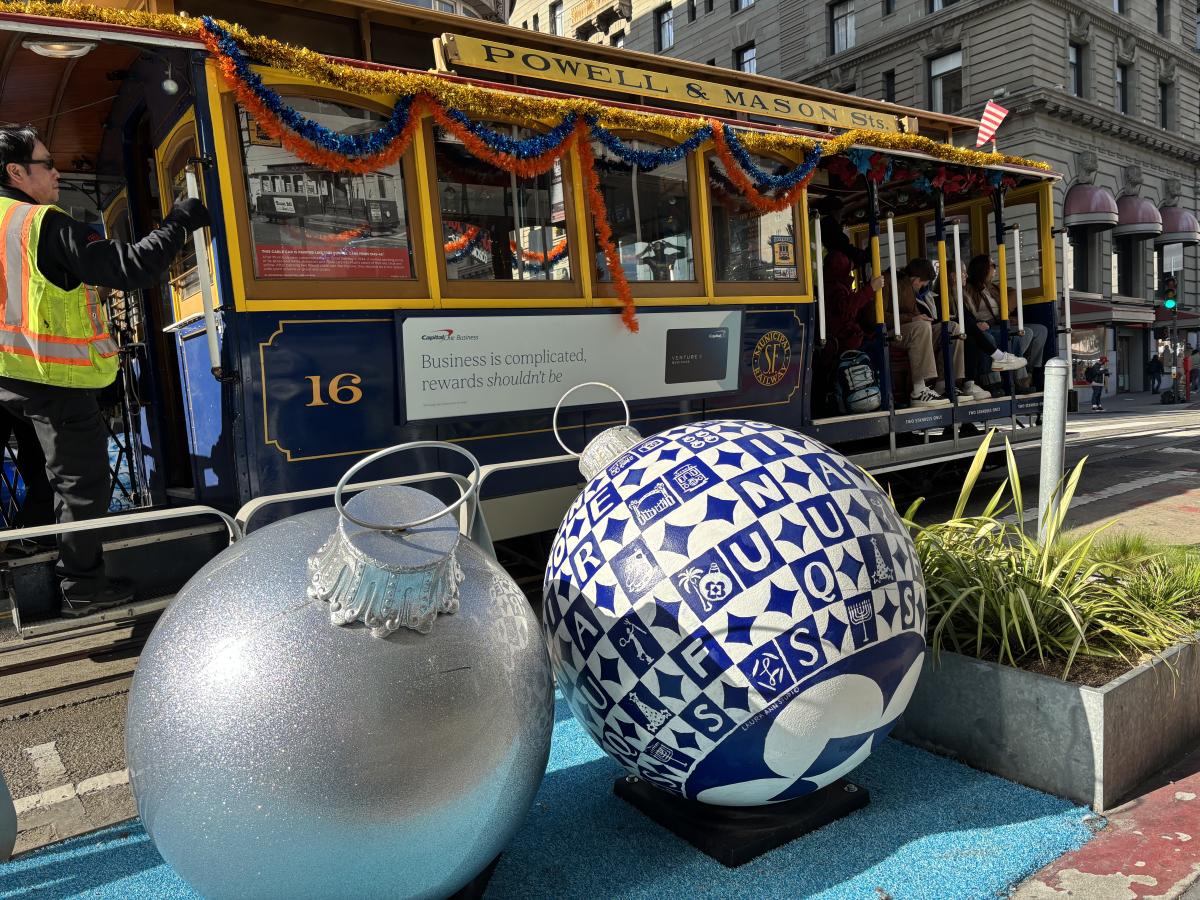 A cable car behind large holiday decorations on a sidewalk.